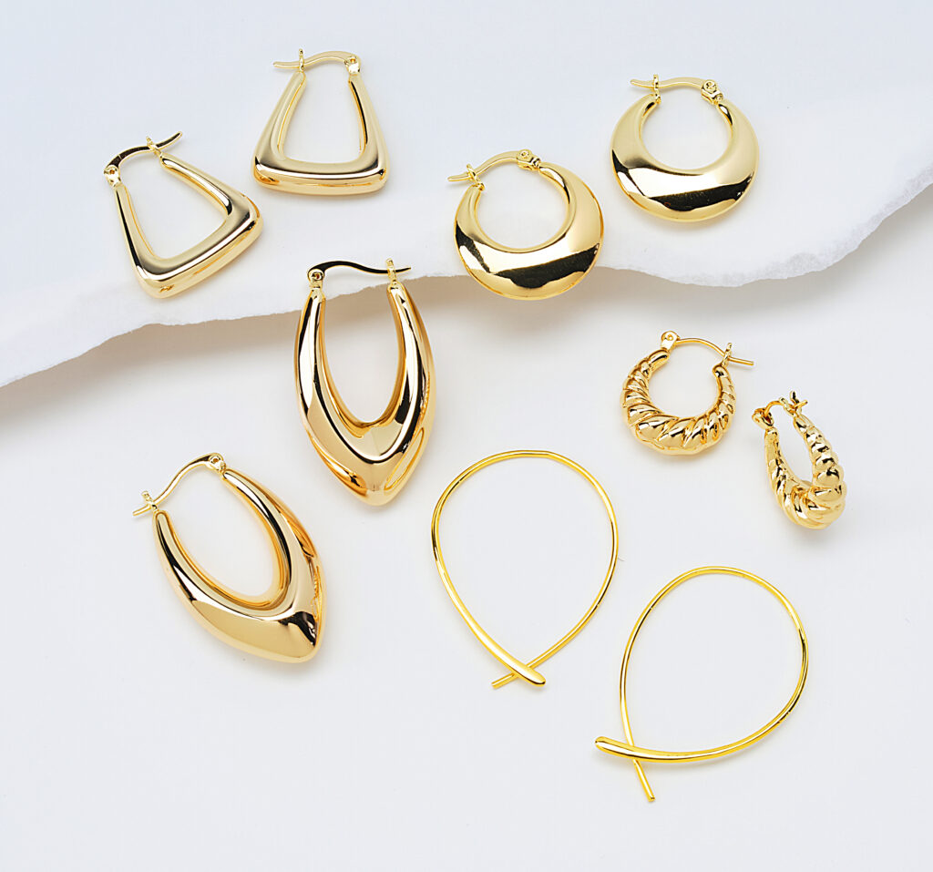 assorted gold earrings on neutral background with soft shadows