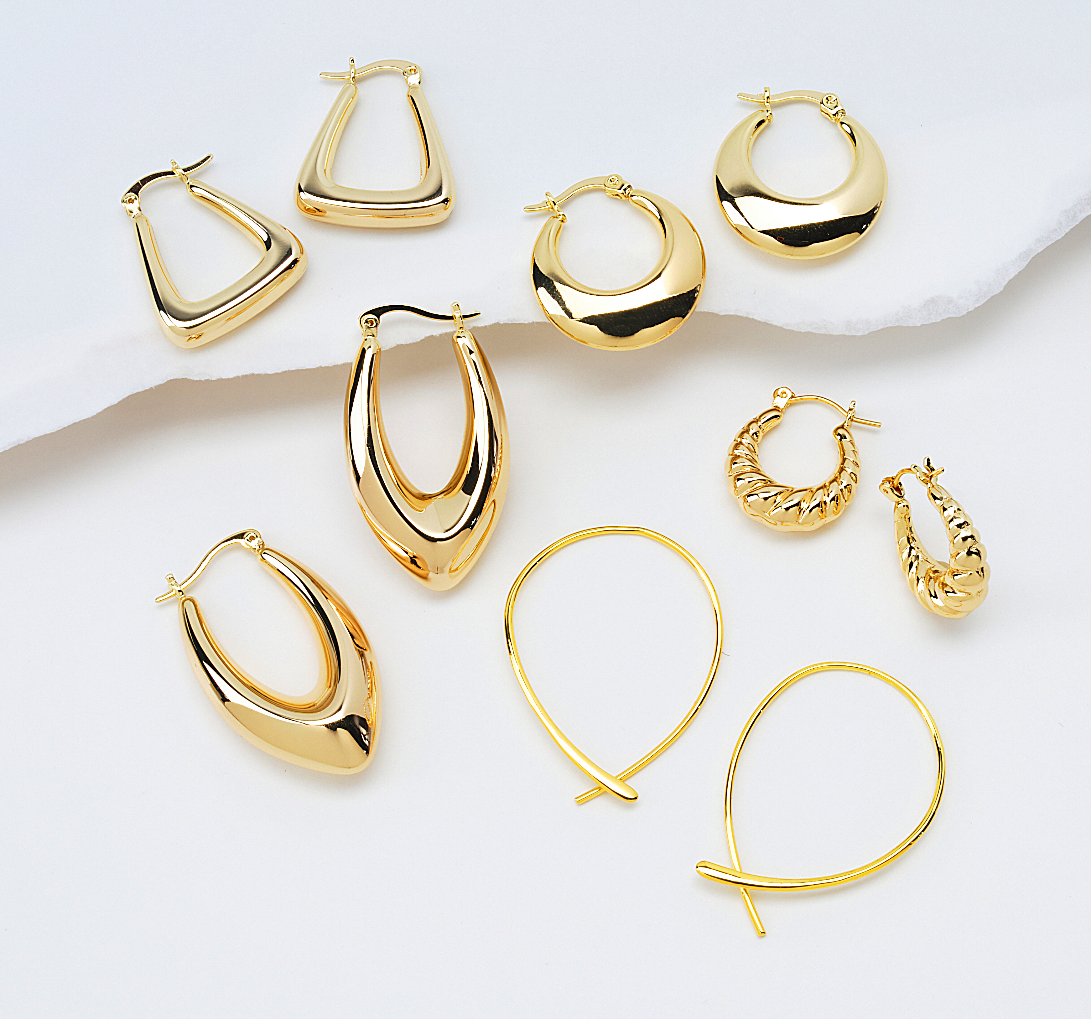assorted gold earrings on neutral background with soft shadows
