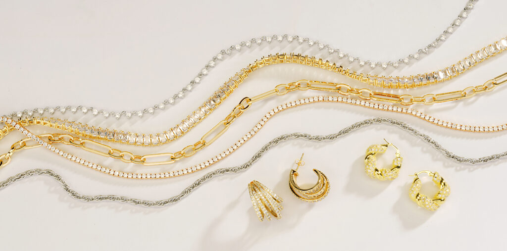 assorted gold and silver jewelry on neutral background with dramatic shadows