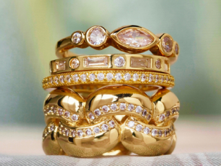 stack of gold and diamond rings on soft green and taupe fabric background