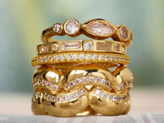 stack of gold and diamond rings on soft green and taupe fabric background