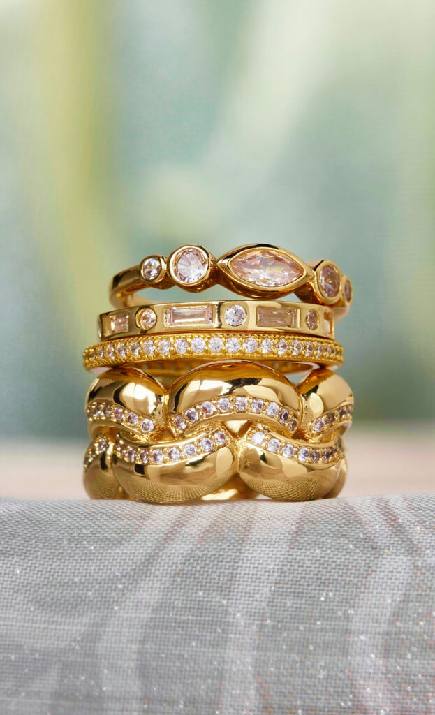 stack of gold and diamond rings on soft green and taupe fabric background