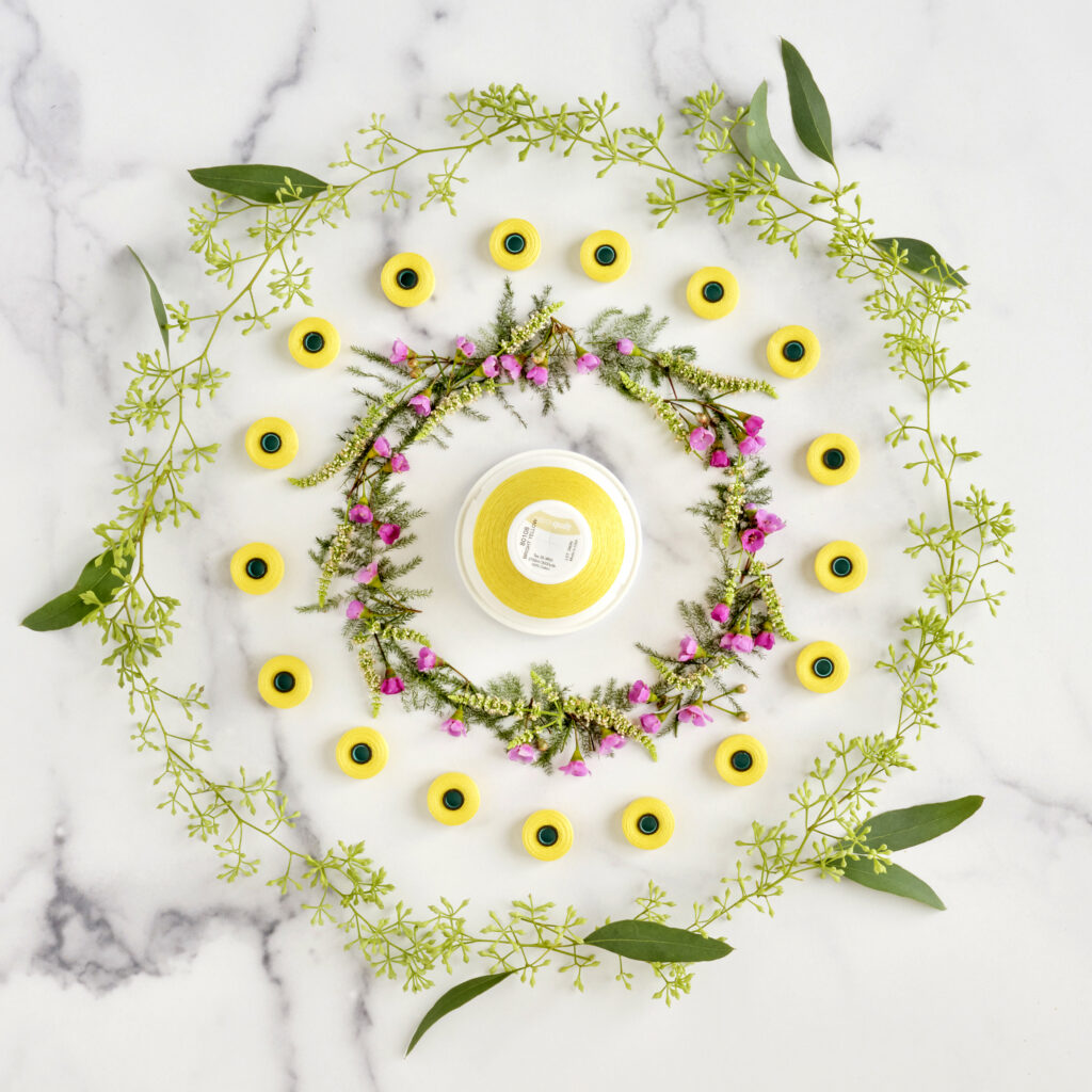wild flowers and eucalyptus in circle arrangement on marble background surrounding a yellow spool of thread