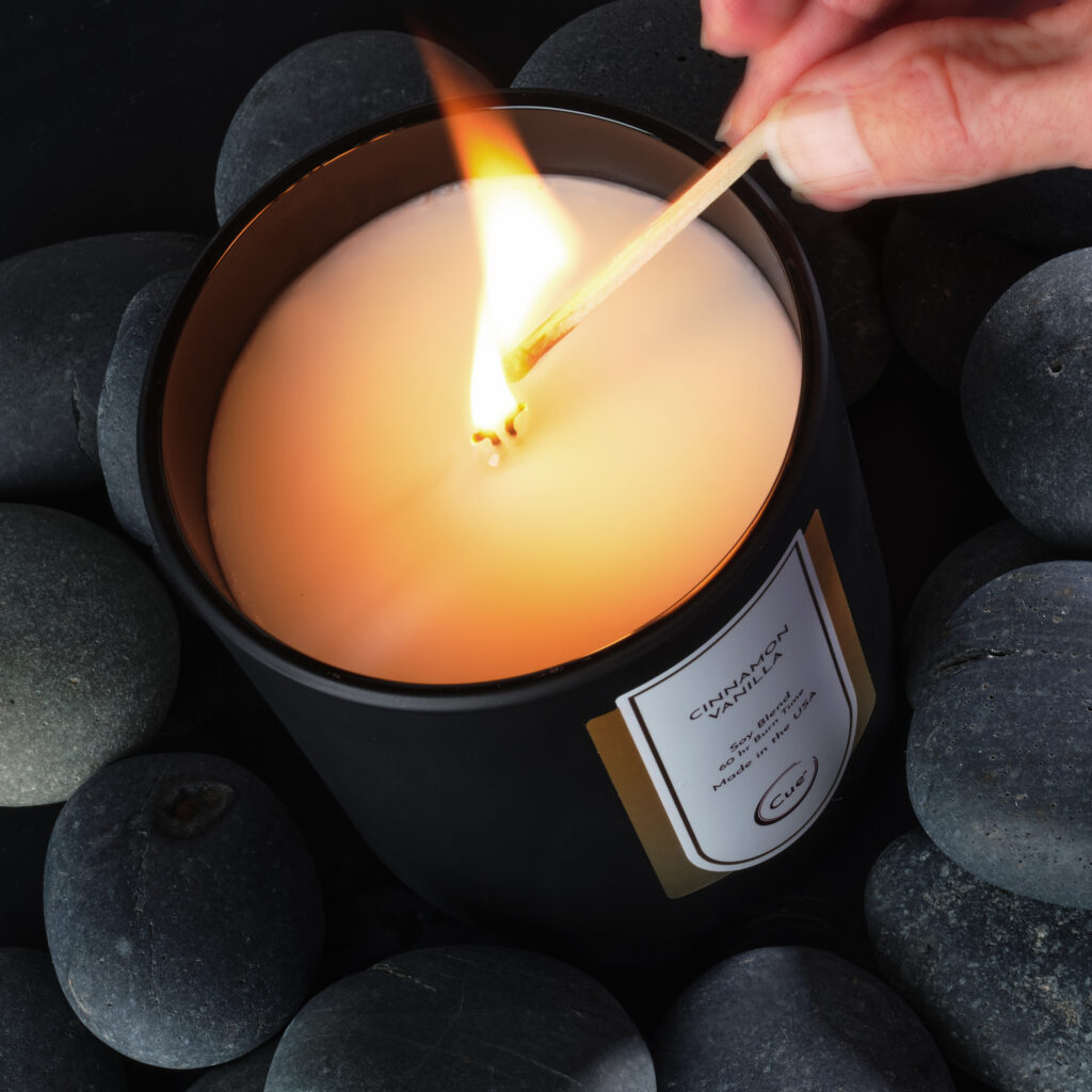 Cue Candle Company Cinnamon Vanilla candle on black stones being actively lit