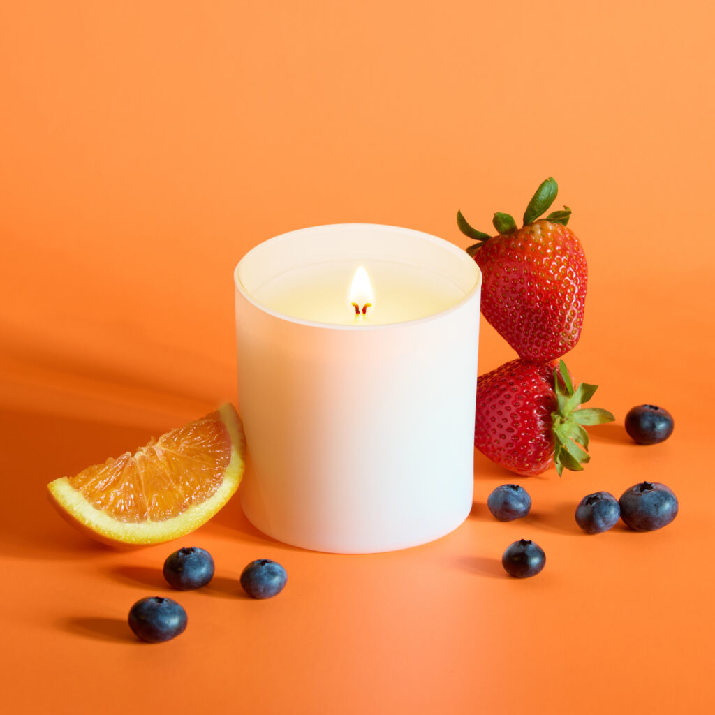 Cue Candle Company white candle jar on orange background with fresh fruit