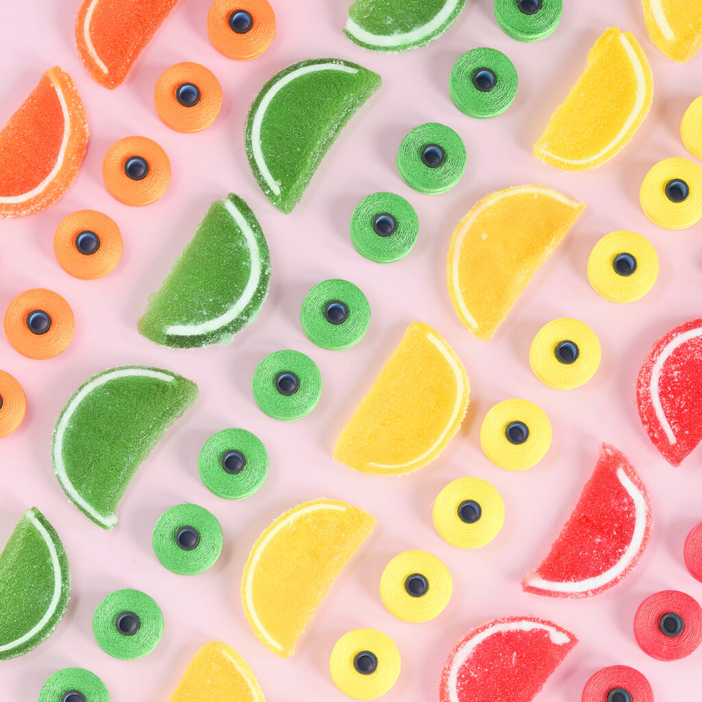 colorful fruit slice candy and bobbins in rows on pink background