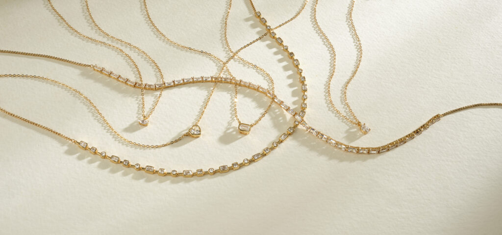 assorted gold and diamond chains and pendants on neutral colored background with dramatic lighting