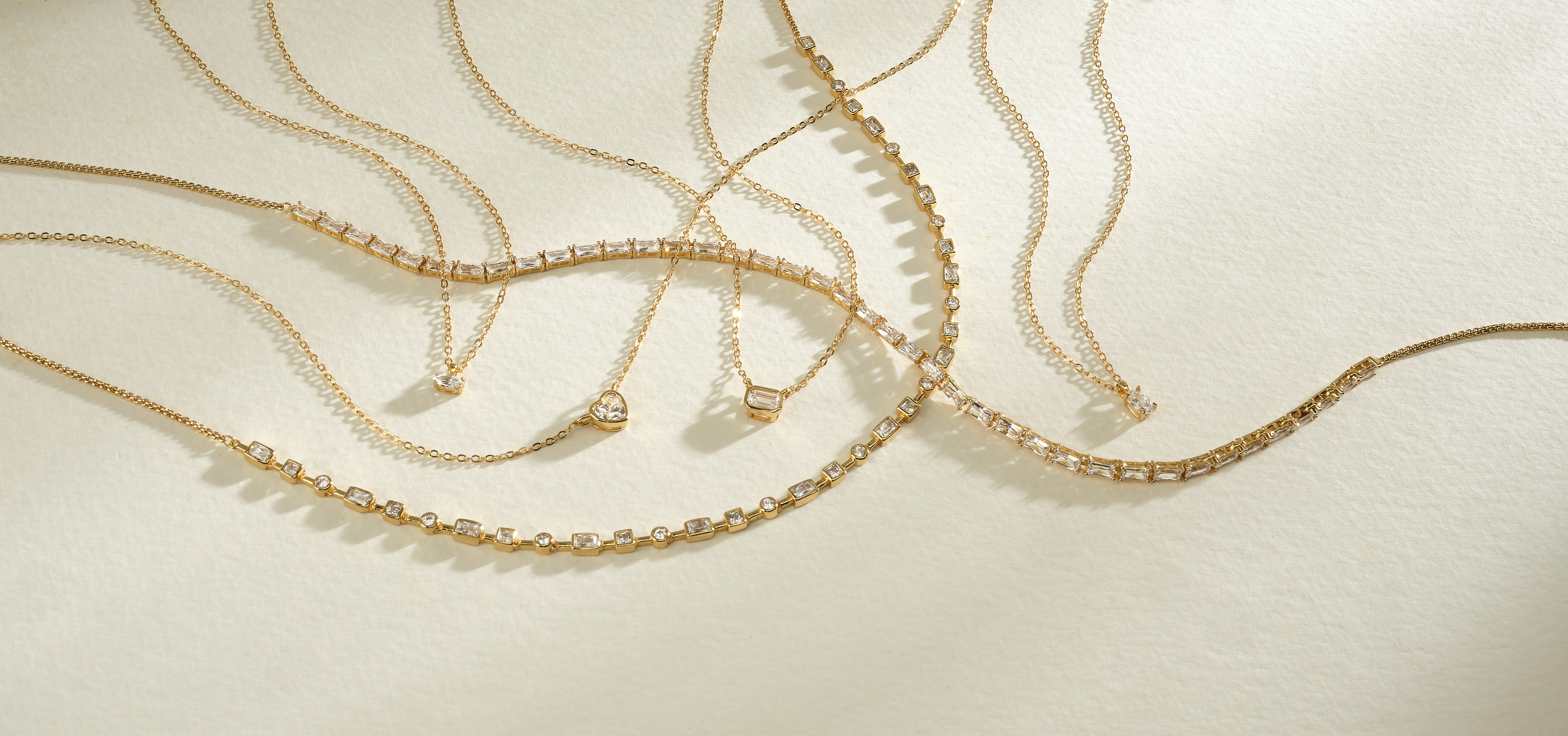 assorted gold and diamond chains and pendants on neutral colored background with dramatic lighting