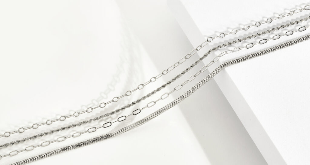 assorted silver chains on neutral colored background with dramatic lighting