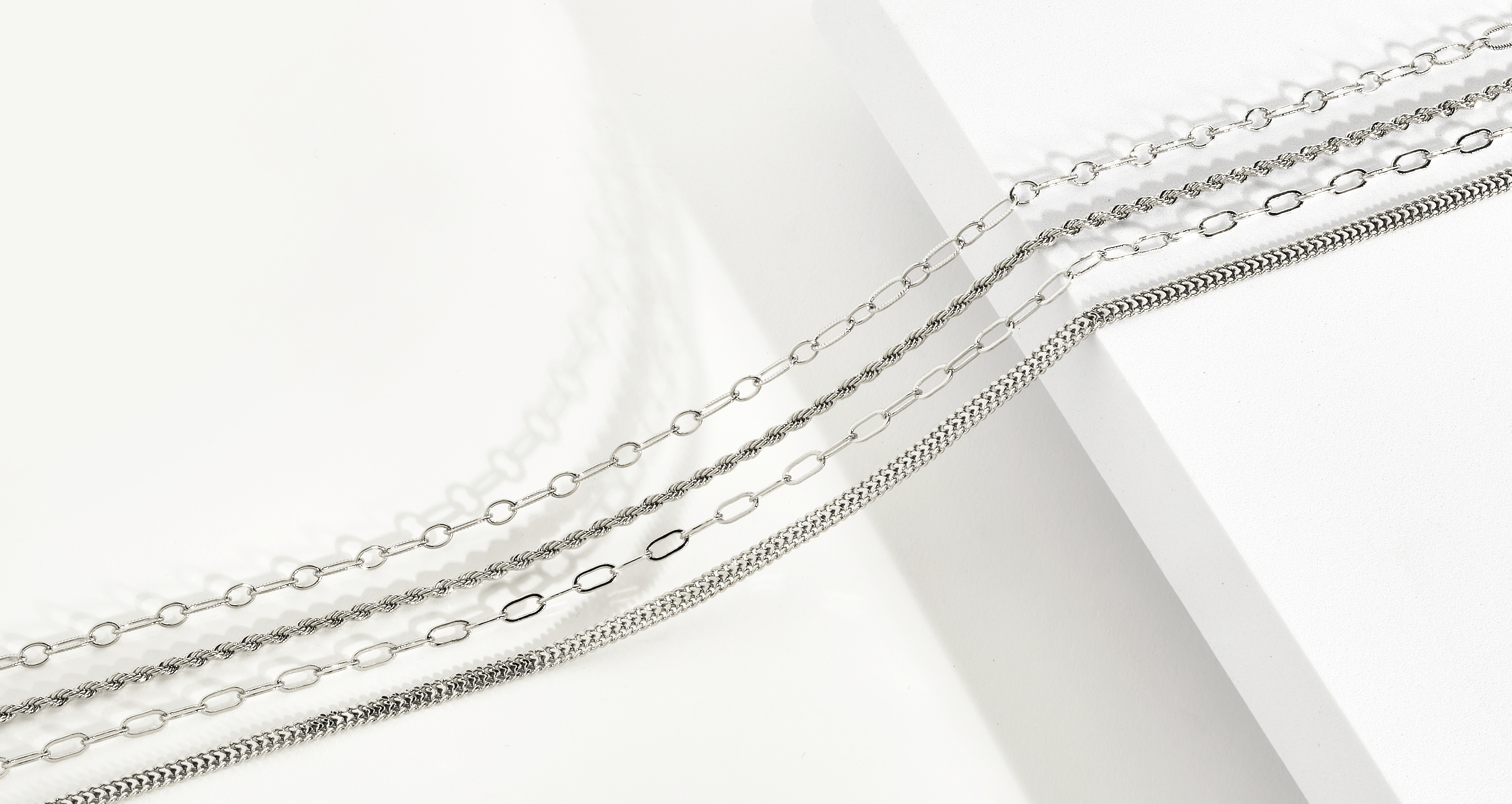 assorted silver chains on neutral colored background with dramatic lighting