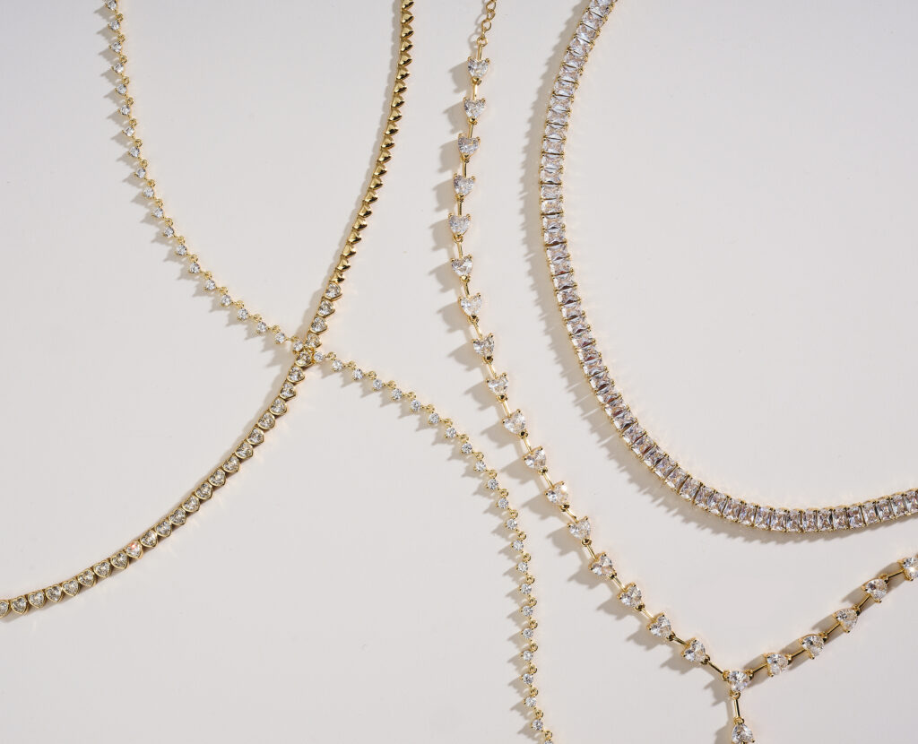 assorted gold and diamond chains and pendants on neutral colored background with dramatic lighting
