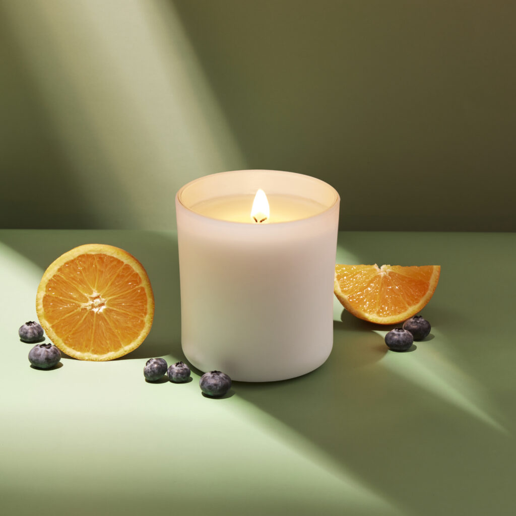 Cue Candle Company white candle jar on green backgrouns with fruit and dramatic lighting