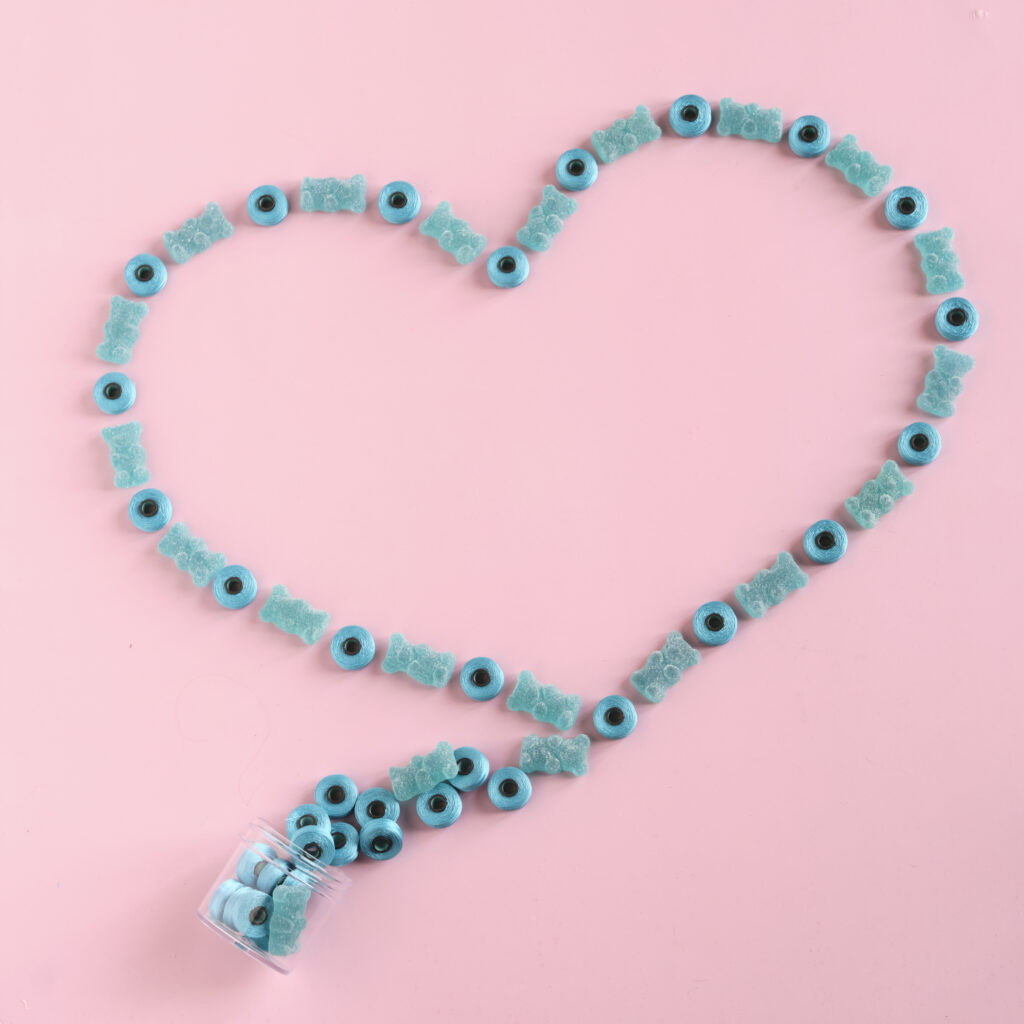 aqua colored gummy bears and bobbins arranges in the shape of a heart on a pink background
