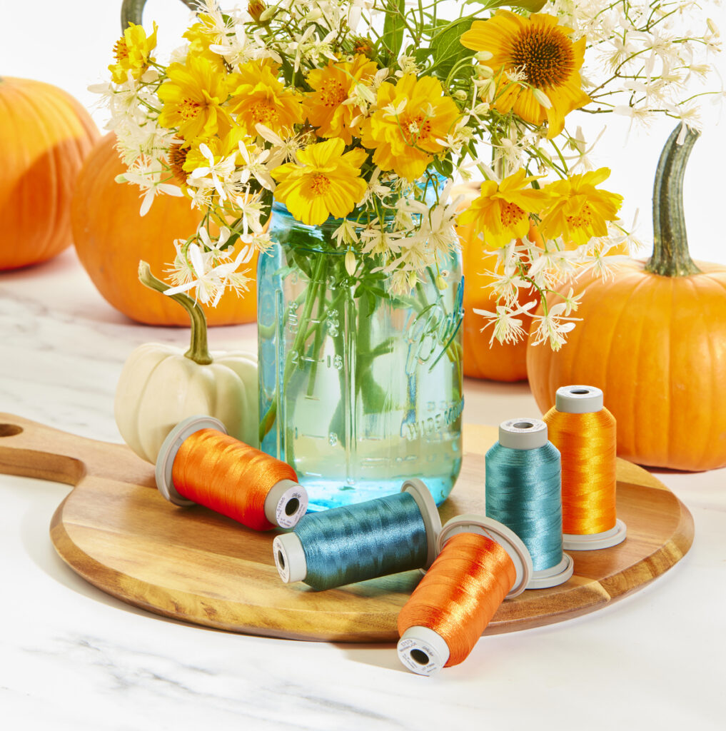 vibrant orange and aqua spools of thread with blue canning jar, pumpkins and wild flowers