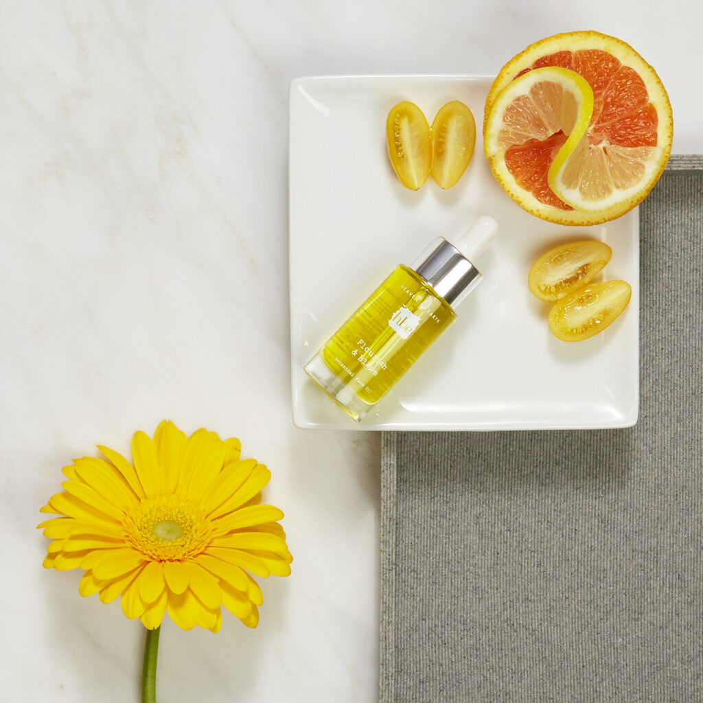 luxury beauty brand botanical oil on white plate with yellow daisy and fruit