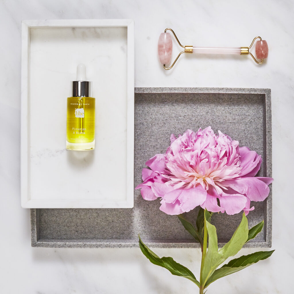 luxury beauty brand botanical oil and rose quartz roller on white with pink peony