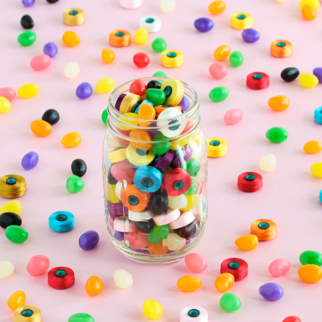 colorful jar full of jelly beans and bobbins which are scattered over the pink background