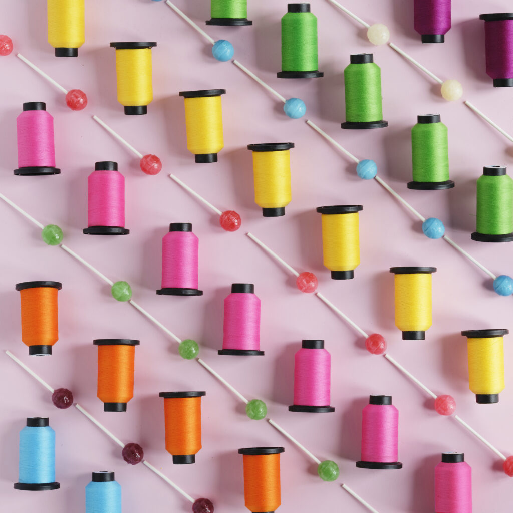 lollipops and spools of colorful thread arranged in rows on pink background