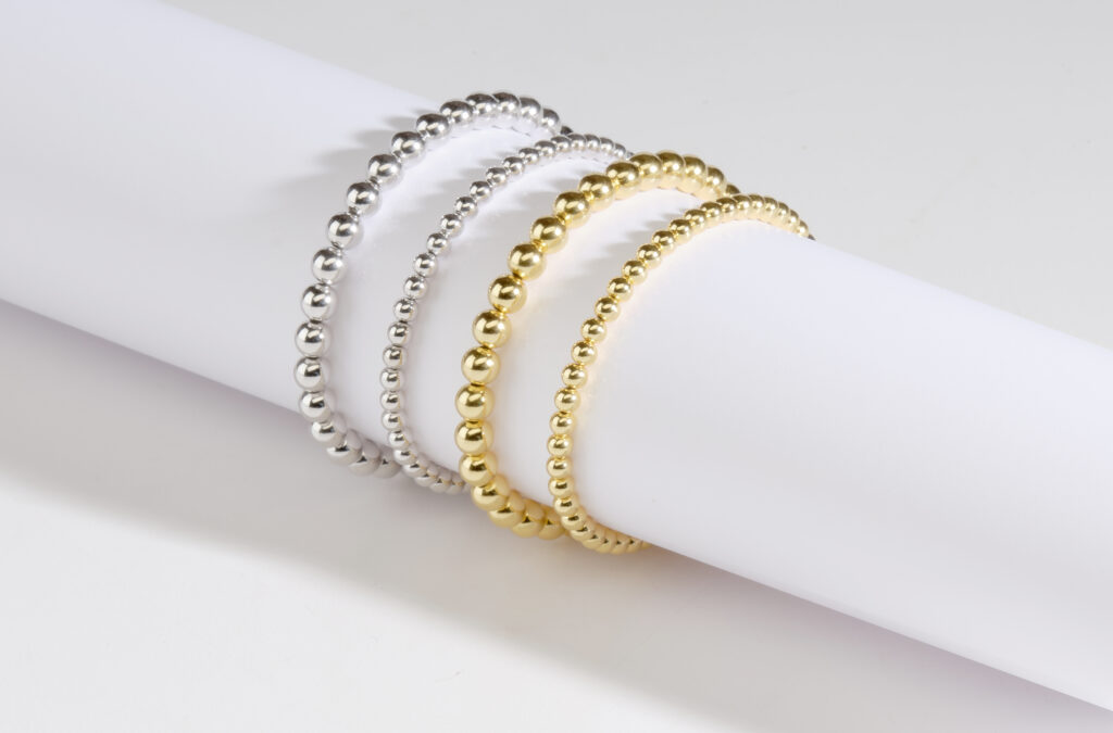 silver and gold beaded bracelets on white tube with shadows
