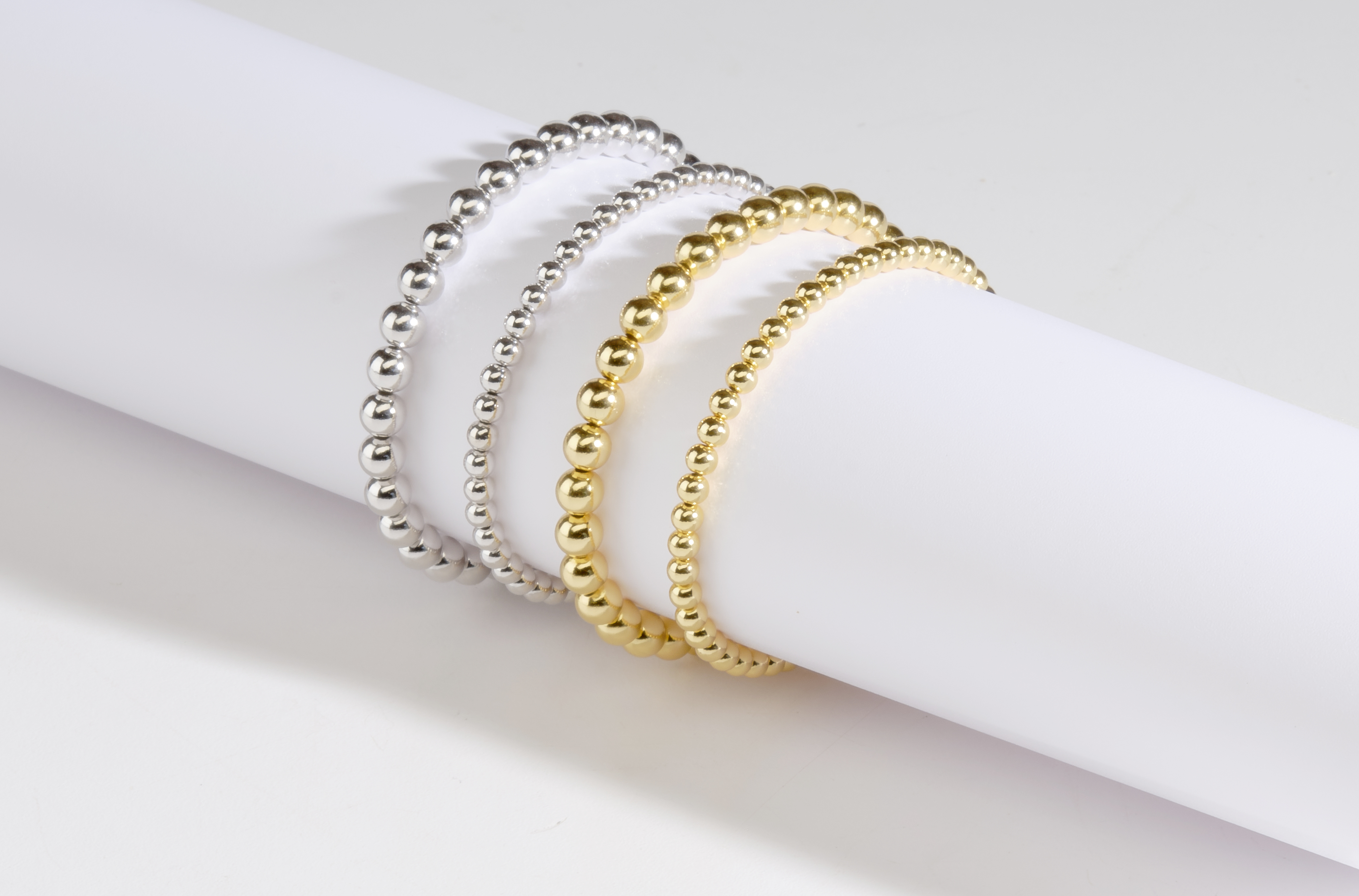 silver and gold beaded bracelets on white tube with shadows