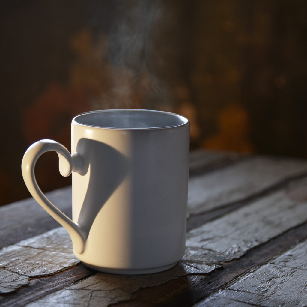 steaming cup of hot coffee with dramatic lighting that forms a heart