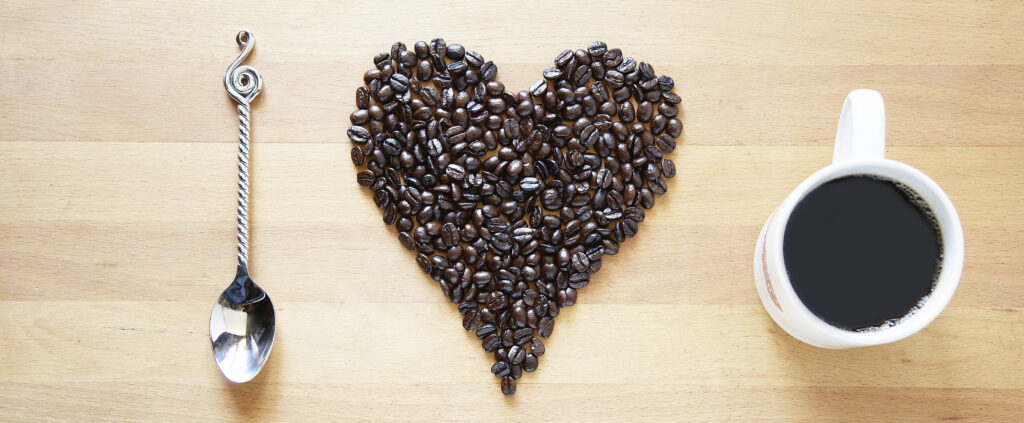 silver spoon coffee beans in shape of heart and cup of coffee viewed from above