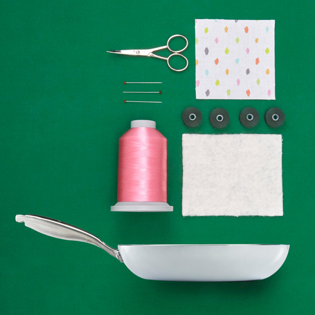 white pan with fabrics scissors pins and thread on a geen backgound