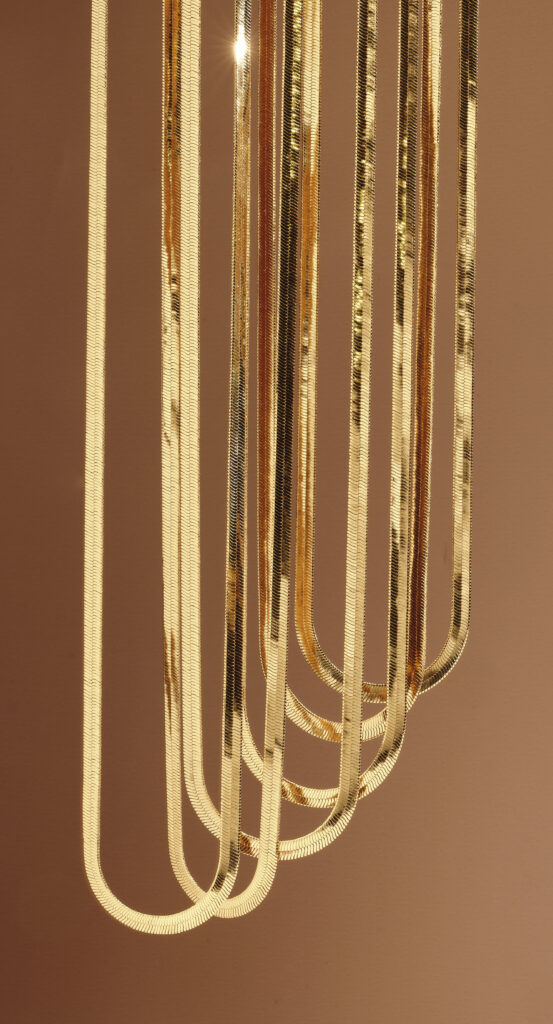 gold herringbone necklaces hanging in front of a brown background