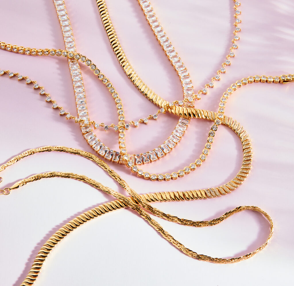 assorted gold and diamond chain on pink colored background with dramatic lighting
