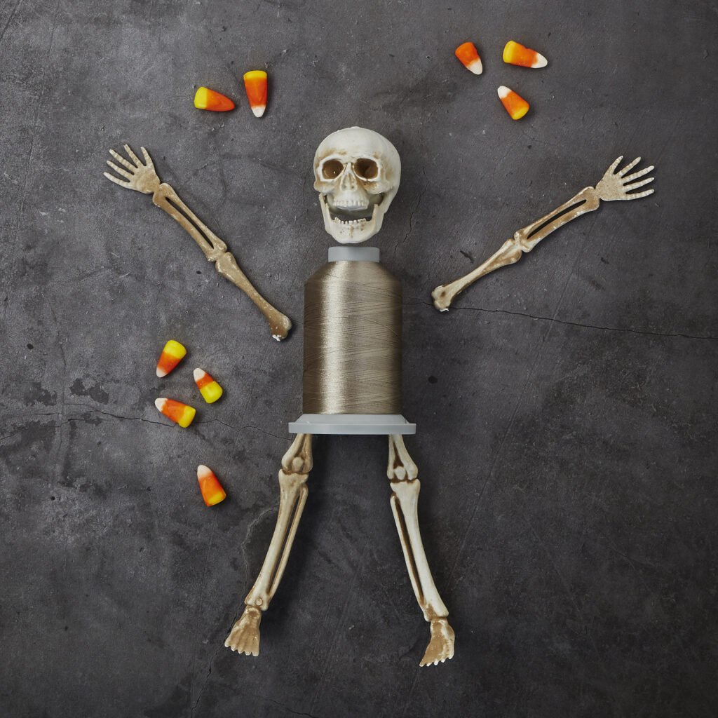 silver spool of thread in whimsical halloween scene of a skeleton and candy corn