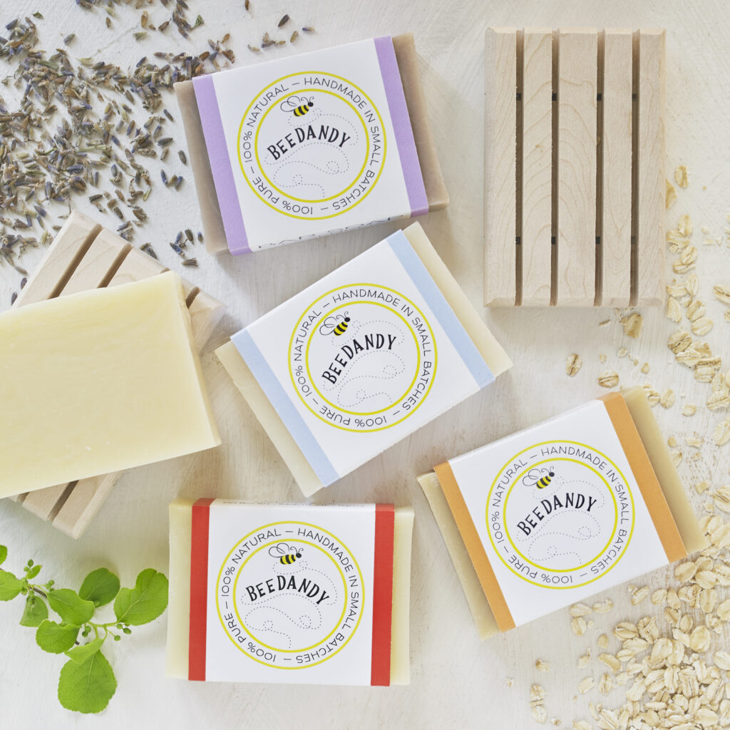 BeeDandy hand crafted soaps on light neutral background with scattered botanicals