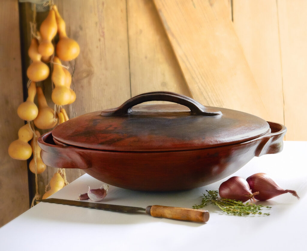 luminous clay vessel for paella with fresh herbs and rustic background