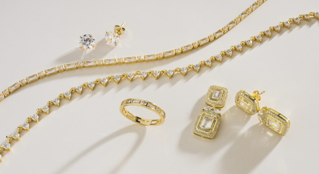 assorted gold and diamond jewelry on neutral colored background with dramatic lighting