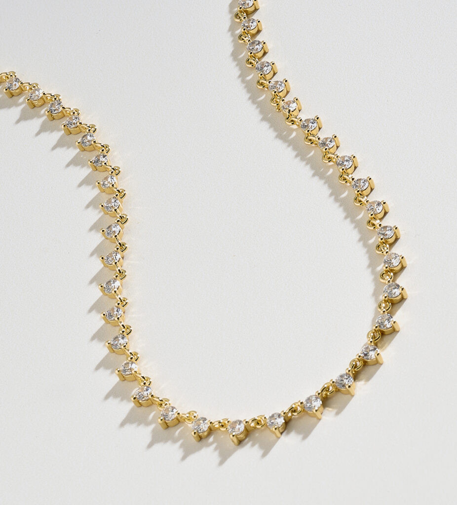 gold and diamond tennis necklace on neutral background with dramatic shadows