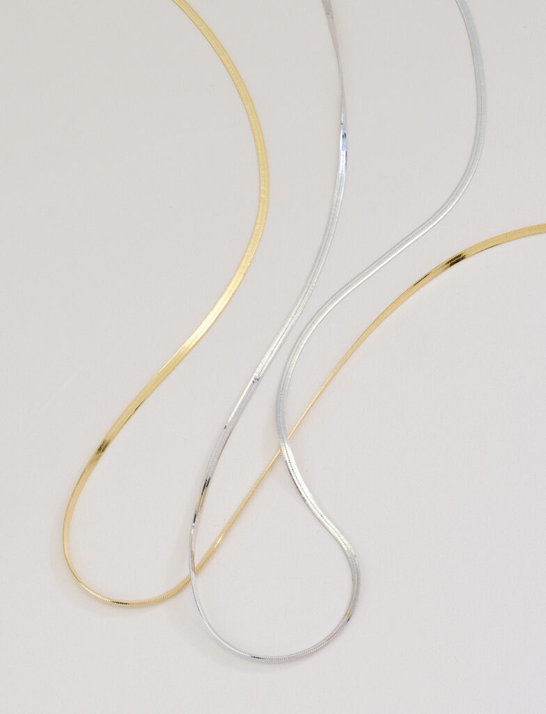 silver and gold herringbone necklaces on neutral background with soft shadows