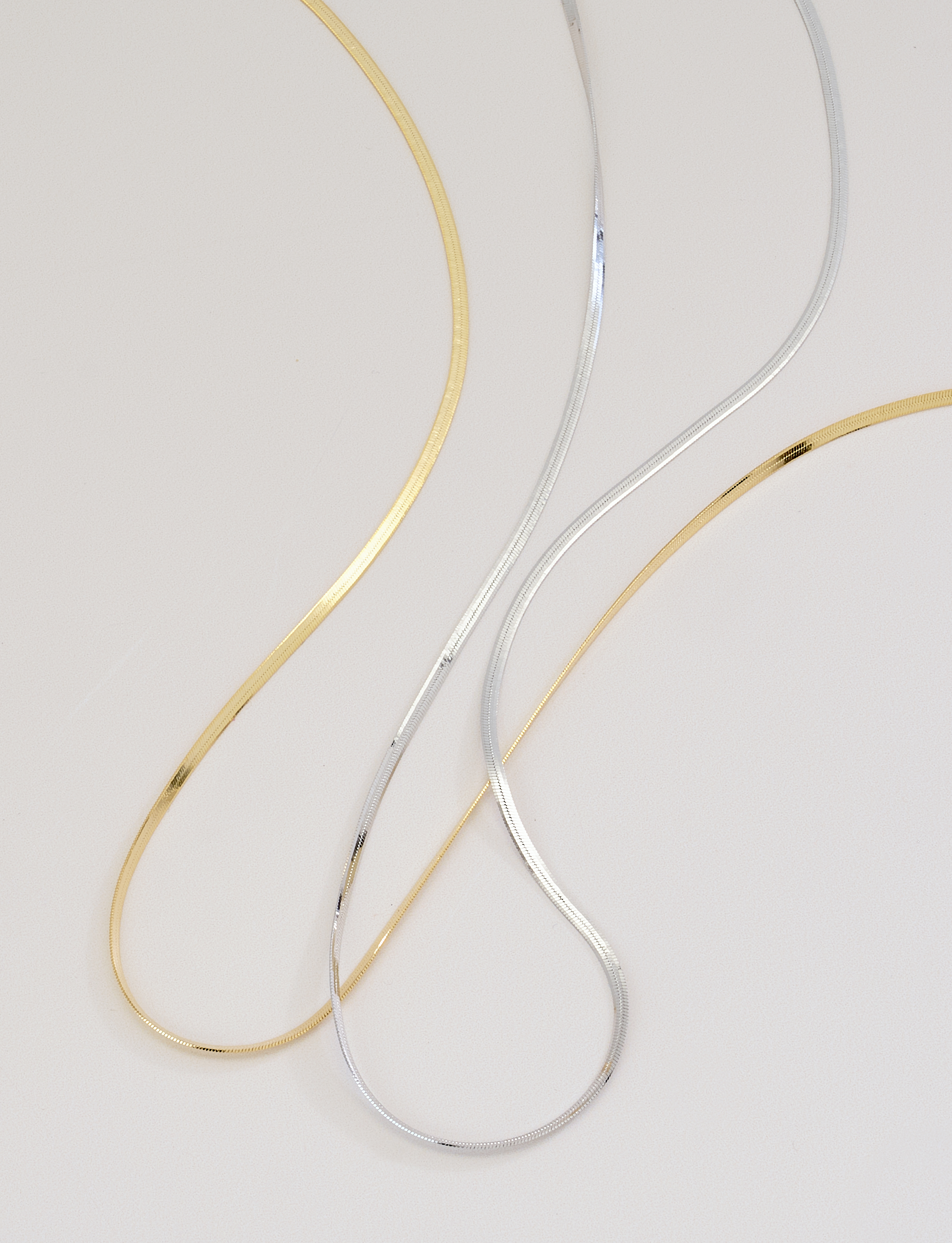 silver and gold herringbone necklaces on neutral background with soft shadows
