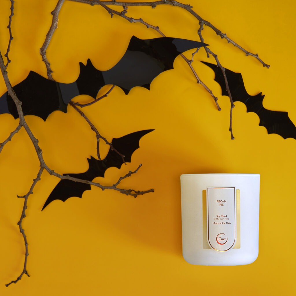 Cue Candle Company white candle jar on orange background with bat silhouette