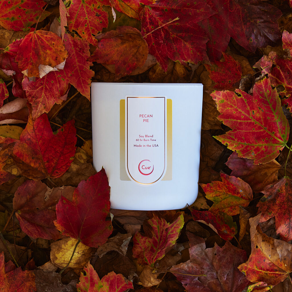 Cue Candle Company white Pecan pie candle laying in red fall leaves