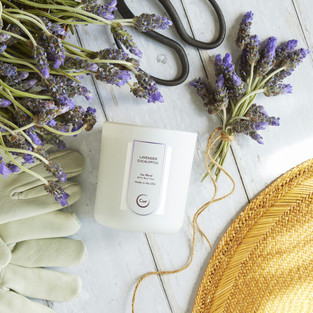 Cue Candle Company white candle on white wood with fresh lavender and gardening tools